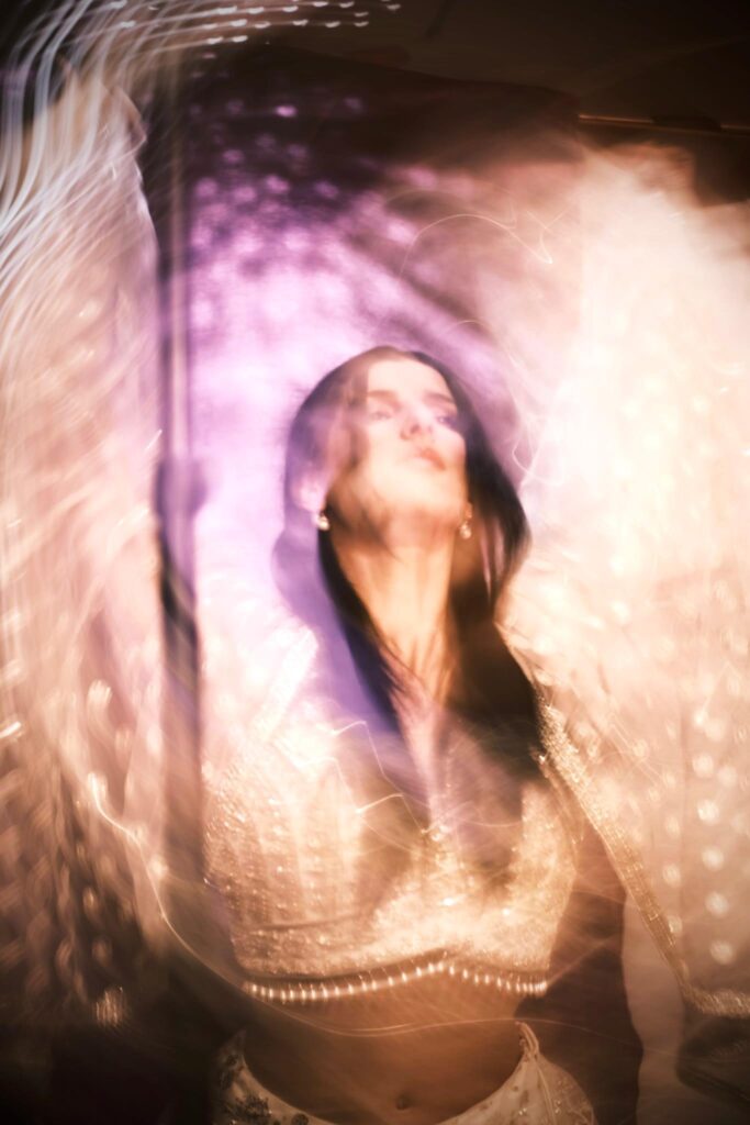 Accueil 4 Portrait artistique de Manal Cherki entourée de faisceaux lumineux en mouvement. Elle regarde vers le haut avec sérénité, portant une tenue délicatement ornée de perles, dégageant une aura de paix.